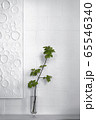 White brick wall with a white artwork and a green branch in a glass vase 65546340