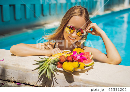 Young woman relaxing and eating fruit plate by the hotel pool. Exotic summer diet. Photo of legs Young woman relaxing and eating fruit plate by the hotel pool. Exotic summer diet. Photo of legs 65551202