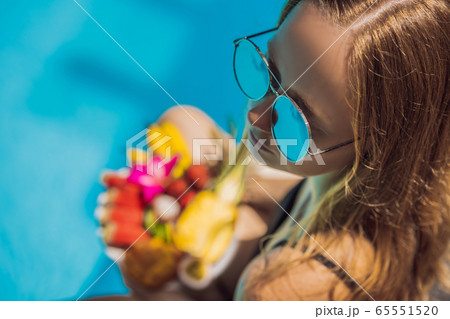 Young woman relaxing and eating fruit plate by the hotel pool. Exotic summer diet. Photo of legs Young woman relaxing and eating fruit plate by the hotel pool. Exotic summer diet. Photo of legs 65551520