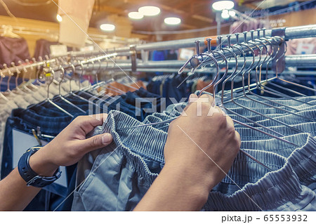 People check and choose pants to buy on hangers in a clothing store. Selective focus on left hand. 65553932