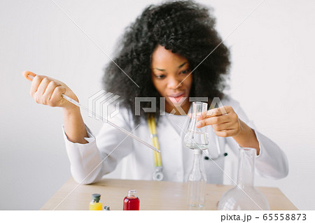 Portrait of a young beautiful African American girl researcher chemistry student carrying out research in a chemistry lab. Scientist analyzing a test-tube. Portrait of a young beautiful African American girl researcher chemistry student carrying out research in a chemistry lab. Scientist analyzing a test-tube. 65558873