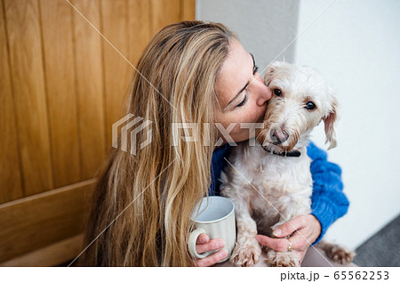 Mature woman relaxing outdoors by front door at home with coffee and pet dog. Mature woman relaxing outdoors by front door at home with coffee and pet dog. 65562253