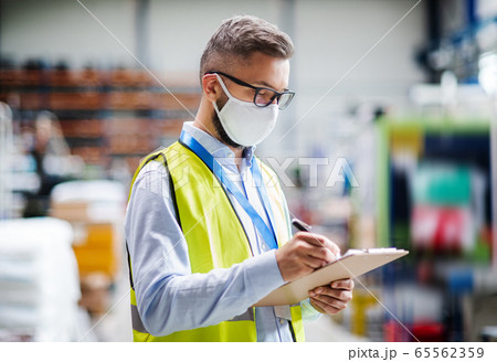 Technician or engineer with protective mask working in industrial factory, writing. Technician or engineer with protective mask working in industrial factory, writing. 65562359