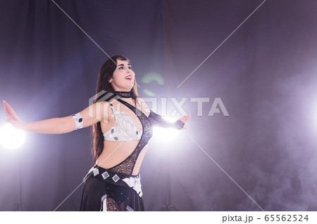 Young woman belly dancer in exotic dress with gold, dancing tribal fusion dance in studio. Copy space. Young woman belly dancer in exotic dress with gold, dancing tribal fusion dance in studio. Copy space. 65562524