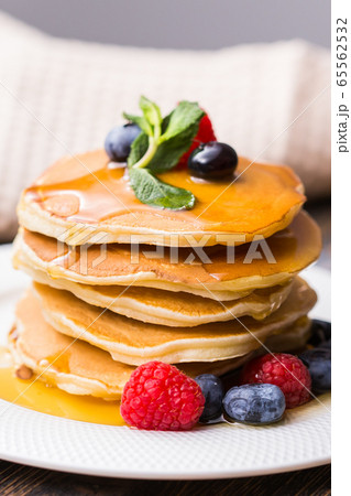 Pile of pancakes with blueberries and raspberries and maple syrup for breakfast on wooden table. 65562532