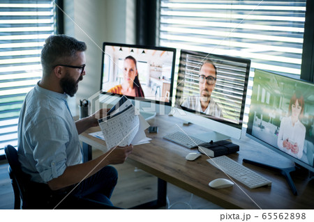 Side view of businessman sitting at desk, having video call. 65562898