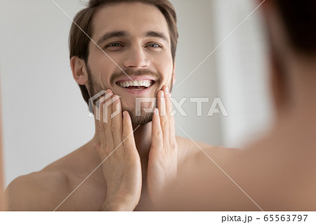 Smiling Caucasian man look in mirror touching face Smiling Caucasian man look in mirror touching face 65563797