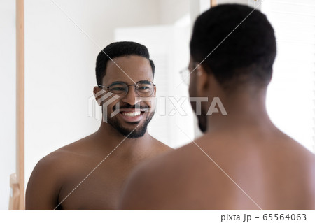 Smiling biracial man in glasses look in mirror in bathroom 65564063