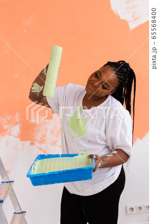 Lovely african american housewife painting wall. Renovation, redecoration and repair concept. Lovely african american housewife painting wall. Renovation, redecoration and repair concept. 65568400