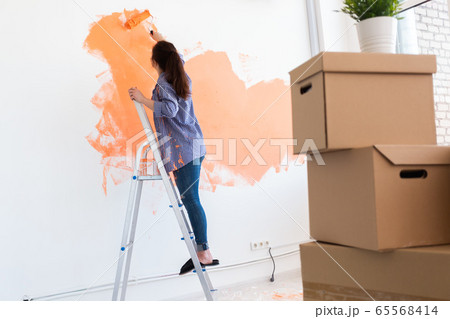 Beautiful woman painting wall in her new apartment. Renovation and redecoration concept. Beautiful woman painting wall in her new apartment. Renovation and redecoration concept. 65568414
