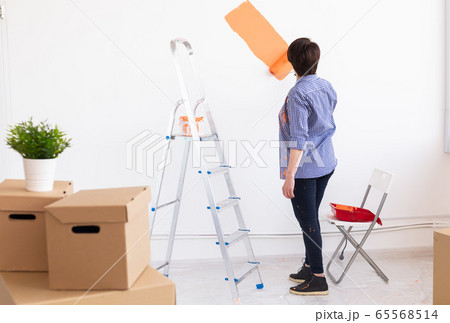 Happy middle-aged woman painting interior wall with paint roller in new house. A woman with roller applying paint on a wall. Happy middle-aged woman painting interior wall with paint roller in new house. A woman with roller applying paint on a wall. 65568514