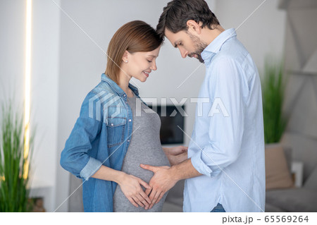 Young dark-haired man touching his wifes pregnant abdomen 65569264