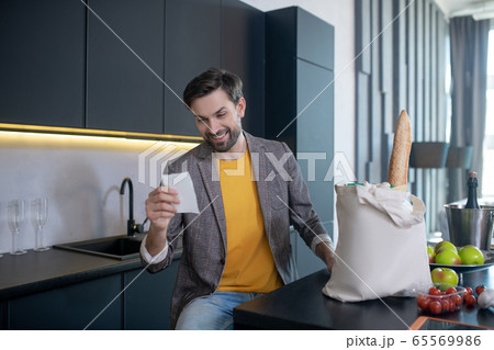 Young bearded man looking at the bill in his hand an smiling 65569986