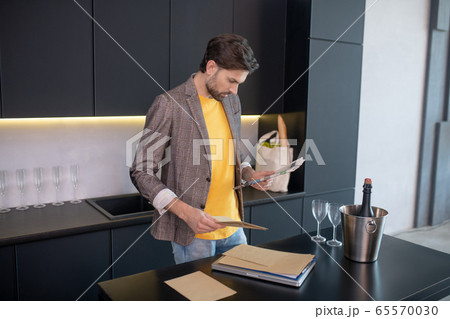 Young bearded man reading a newspaper and looking worried Young bearded man reading a newspaper and looking worried 65570030