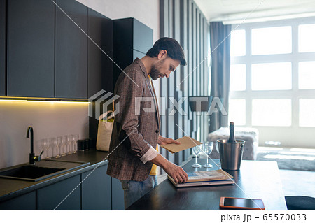 Young bearded man holding an envelope in his hand and looking concentrated Young bearded man holding an envelope in his hand and looking concentrated 65570033