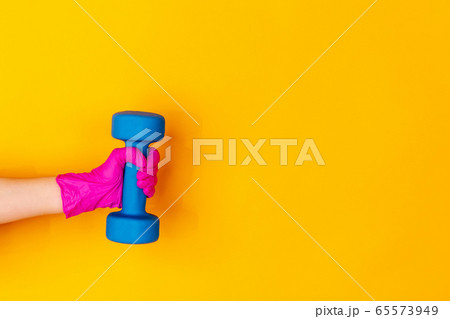 Hand in pink rubber glove holding dumbbell, gym weight isolated on yellow studio background with copyspace. 65573949