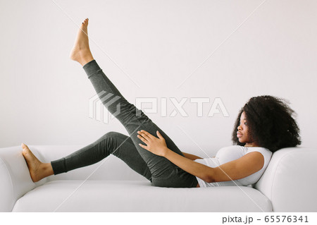 An African American young woman lying on a white bed and doing physical exercises An African American young woman lying on a white bed and doing physical exercises 65576341