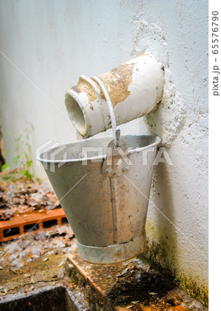 Vertical color image with a side view of a vintage metal bucket hanging from an outside faucet Vertical color image with a side view of a vintage metal bucket hanging from an outside faucet 65576790
