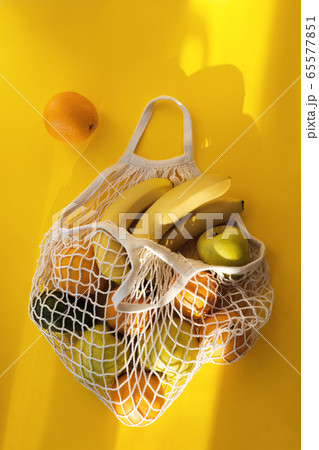 Oranges, Bananas, Apples, Avocados lie in string bag on bright yellow background and hard sunshine. The concept of zero waste. Using reusable bags instead of disposable cellophane packets. 65577851