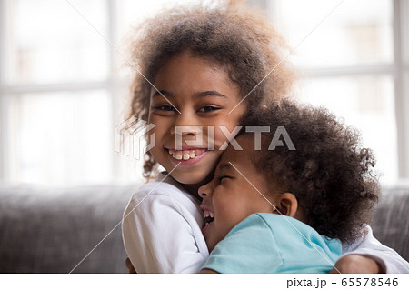 Happy african american sister embracing little brother looking a Happy african american sister embracing little brother looking a 65578546