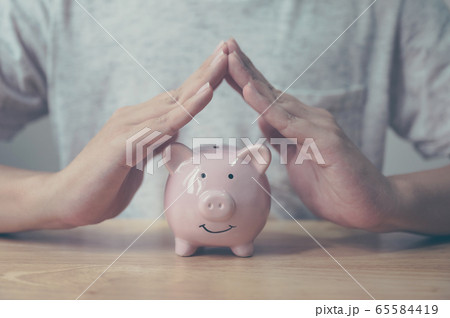 Man hand protect piggy bank on wood table Man hand protect piggy bank on wood table 65584419