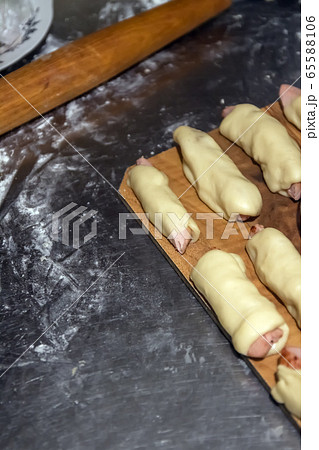 Prepared raw sausages in the test before baking lie on a table under a napkin. Concept, home cooking Prepared raw sausages in the test before baking lie on a table under a napkin. Concept, home cooking 65588106