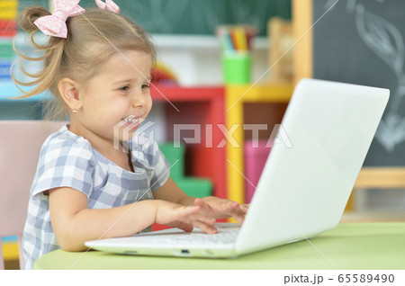 Portrait of curious little girl using laptop at desk Portrait of curious little girl using laptop at desk 65589490