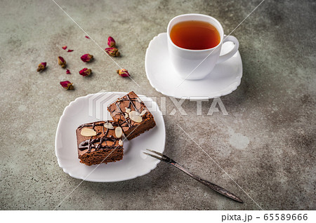 Homemade brownie with almonds on a saucer with a fork on wooden table. Next cup of tea and rose buds Homemade brownie with almonds on a saucer with a fork on wooden table. Next cup of tea and rose buds 65589666