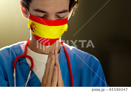 Doctor in face mask praying for Spain. 65590347