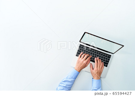 白い背景の上でノートパソコンを使う男性。俯瞰撮影、左側に余白。 65594427