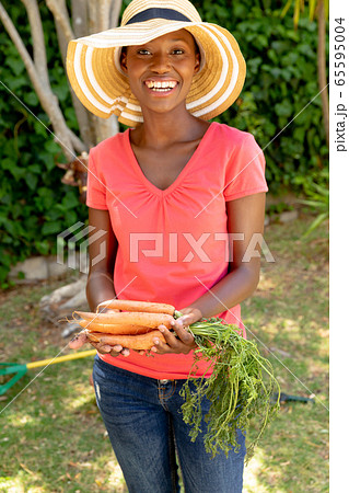 African American woman wearing gloves and presenting fresh carrots African American woman wearing gloves and presenting fresh carrots 65595004