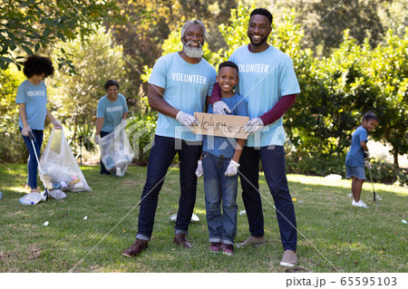 Multi-generation people collecting garbage with a boy holding a sign written Volunteer 65595103