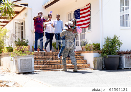 African American male soldier wearing uniform and his family standing by their house 65595121