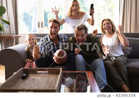 Multi-generation Caucasian family sitting on a couch together and watching a game Multi-generation Caucasian family sitting on a couch together and watching a game 65595358