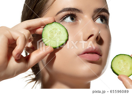 Freshness. Close up of beautiful young woman with cucumber's slices on her face on white background. Cosmetics and makeup, natural and eco treatment, skin care. Freshness. Close up of beautiful young woman with cucumber's slices on her face on white background. Cosmetics and makeup, natural and eco treatment, skin care. 65596089