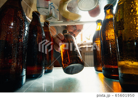 Caucasian man takes cold refreshing beer from out the fridge, inside view from fridge of hand holding the bottle Caucasian man takes cold refreshing beer from out the fridge, inside view from fridge of hand holding the bottle 65601950
