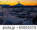 夕焼けでオレンジ色に染まる空と富士山と波しぶき 65603379