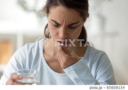 Unhappy lady feeling unwell, getting aspirin or painkiller. Unhappy lady feeling unwell, getting aspirin or painkiller. 65609134