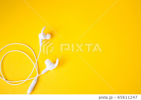 White headphones with a wire on a yellow background. Concept of gadgets. 65611247
