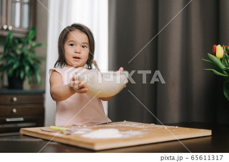 Beautiful little two-year-old girl wearing white dress is holding hands transparent bowl 65611317