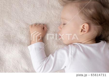 Childhood, sleep, rest, family, lifestyle concept - close-up portrait of a cute little boy of 2 years old in a white body sleeping on a beige bed at noon with mouth open top and side view. Childhood, sleep, rest, family, lifestyle concept - close-up portrait of a cute little boy of 2 years old in a white body sleeping on a beige bed at noon with mouth open top and side view. 65614731