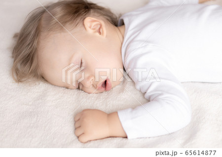 Childhood, sleep, rest, family, lifestyle concept - close-up portrait of a cute little boy of 2 years old in a white body sleeping on a beige bed at noon with mouth open top and side view. 65614877