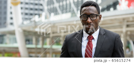 Young handsome African businessman standing in front of modern building at Bangkok city 65615274