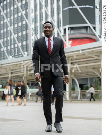 Happy young handsome African businessman walking in the city outdoors 65615276