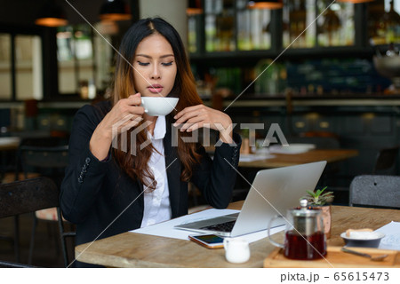 Young beautiful Asian businesswoman drinking coffee at the coffee shop Young beautiful Asian businesswoman drinking coffee at the coffee shop 65615473