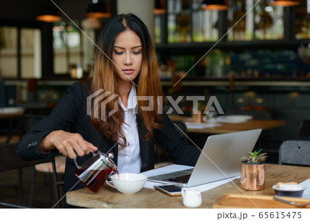 Young beautiful Asian businesswoman drinking coffee at the coffee shop Young beautiful Asian businesswoman drinking coffee at the coffee shop 65615475