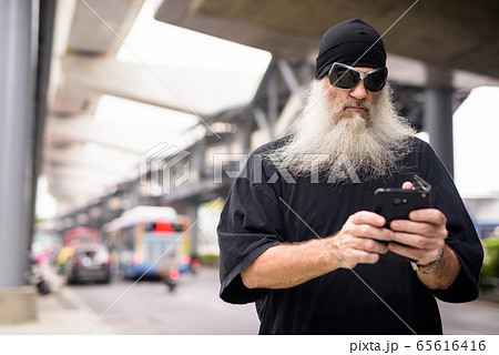 Mature bearded hipster man with sunglasses using phone in the city streets outdoors 65616416