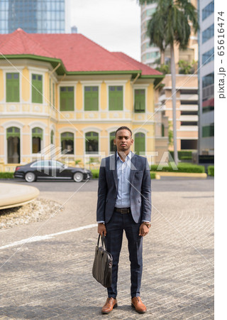 Full body shot of young handsome African businessman with suitcase ready for work outdoors Full body shot of young handsome African businessman with suitcase ready for work outdoors 65616474