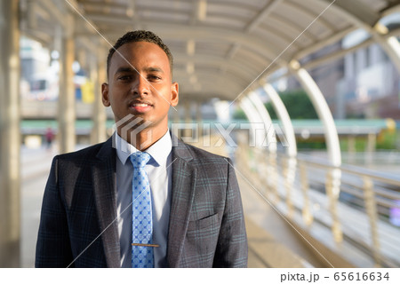 Happy young handsome African businessman in suit smiling in the city 65616634