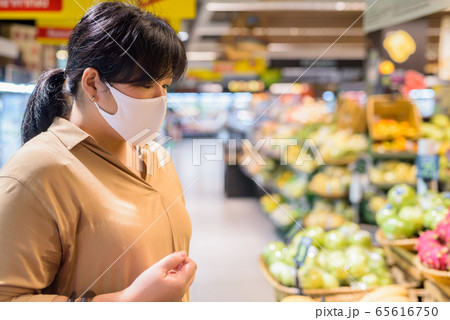 Profile view of overweight Asian woman with mask shopping inside supermarket 65616750